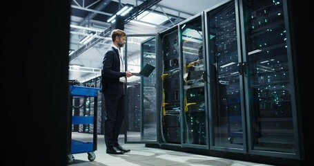 Female System Administrator Passing by Server Racks with a Tablet. Data Center Specialist Running Diagnostics on a Laptop Computer, Optimizing Cybersecurity Protocols in a High-tech Facility