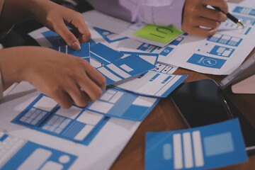 Close up ux developer and ui designer brainstorming about mobile app interface wireframe design on table with customer breif and color code at modern office.Creative digital development agency.