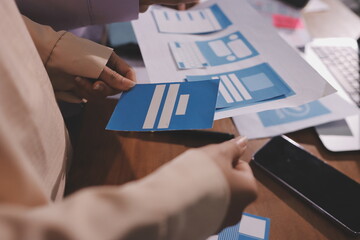 Close up ux developer and ui designer brainstorming about mobile app interface wireframe design on table with customer breif and color code at modern office.Creative digital development agency.