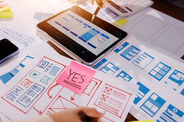 Close up ux developer and ui designer brainstorming about mobile app interface wireframe design on table with customer breif and color code at modern office.Creative digital development agency.
