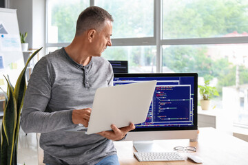 Mature male programmer with laptop in light office