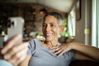 © Marko Geber - Smiling senior woman video calling family on smartphone from cozy home