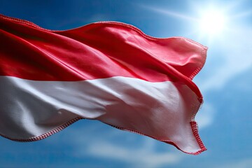 Wall Mural - A red  white flag waves against a blue sky with a bright sun creating highlights