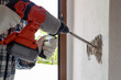 © francescomou - Carpenter electrician with demolition hammer prepares the cavity in the wall where to insert the built-in electrical panel. Work safely with protective gloves. Construction industry.