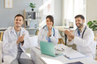 © Studio Romantic - Happy smiling doctors applauding on a meeting sitting at the desk on workplace in clinic. Successful team of young medical staff sitting in hospital on conference. Medicine and health care concept.