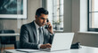 © Kaluya Stock - Concentrated businessman in a suit making a phone call while using his laptop in a modern office, depicting professional communication and multitasking.