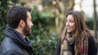 © Keo - A man and a woman standing in a park, wearing winter clothing, with green and brown leaves in the background.