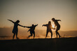 © qunica.com - A group of friends plays and dances on the beach during a captivating sunset, silhouetted against the golden light, evoking feelings of joy, unity, and the beauty of shared moments.