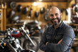 © digitalpochi - A portrait smiling man standing next to a motorcycle on a workbench
