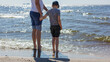 © Linas T - A father and his son were wading barefoot in the water by the sea. Horizontal photo.