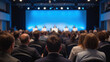 © Oran - Professional audience attentively listens to speakers at conference, with blue lit stage in background. atmosphere is focused and engaging