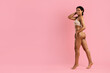 © Anastasiya - Happy African American woman in nude underwear walking confidently with hand on head, smiling against pink background. Feminine, radiant, and full of positive energy.