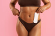 © Anastasiya - Young Black woman in underwear applying pantyliner to panties, showing daily feminine hygiene routine on pink studio background, promoting personal health and cleanliness.
