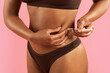 © Anastasiya - Closeup of young African American woman injecting herself in belly with syringe in underwear on pink studio background, illustrating medical procedure or fertility treatment.