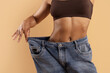 © Anastasiya - Closeup of African American woman in brown underwear showing big jeans, highlighting her slim waist and successful weight loss on beige background.