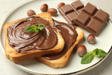 Wall Mural - toasts with tasty chocolate spread, pieces, mint and hazelnuts on light table, closeup