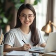 © e_zeynall1 - Smiling Student Studying: A young woman with a radiant smile, wearing glasses, diligently works on her laptop and notebook, exuding confidence and academic success.