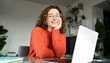 © insta_photos - Portrait of happy young woman or student wearing glasses sitting at desk at home office with laptop computer looking at camera advertising online learning, remote work, business webinars.