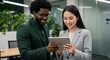 © MdNazim - Smiling business colleagues looking at a tablet together in a modern office environment