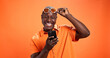 © peopleimages.com - Excited, fashion or black man with phone in studio for surprise discount, sale or bargain deal. Space, notification or happy model on orange background in trendy sunglasses, good news or cool clothes