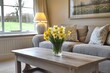 © Ahmads - A bright living room with gray sofas, a wooden coffee table, and yellow daffodils in the vase on top of it. A window is open behind which there's another sofa. The walls have light gray curtains.