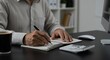 © Imagine Stuff - Man writing in notebook with pen calculator and coffee cup on desk