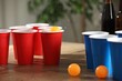 © New Africa - Beer pong game. Plastic cups with drinks and balls on wooden table, closeup