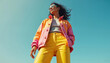 © Maryna - Stylish woman in colorful Y2K fashion. Trendy outfit includes jacket, sunglasses, yellow pants. Girl poses against bright blue sky. High fashion photo embodies modern aesthetics. Fashion blog