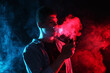 © New Africa - Man using electronic smoking device in neon lights on dark background