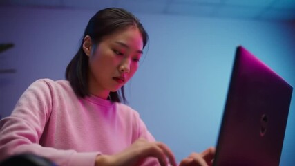 Focused young woman coding on laptop with vibrant neon lighting ambiance