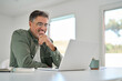 © insta_photos - Smiling wearing eyeglasses looking at computer sitting at table. Happy older mature middle aged man using laptop hybrid working online, elearning, browsing web, searching online at home.