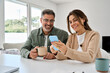 © insta_photos - Smiling mature older man and woman holding cellphone browsing internet, texting message on mobile cell phone technology. Middle aged happy couple using smartphone relaxing at living room table at home