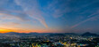 A stunning panoramic view of a coastal city at sunset at Phuket city, showcasing vibrant hues of orange and blue in the sky, with mountains, and urban lights creating a harmonious blend of natural
