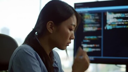 Focused asian software engineer reviewing encrypted code on monitor screen