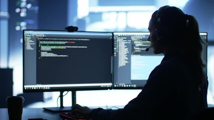 Focused female programmer coding on dual monitors in dimly lit office