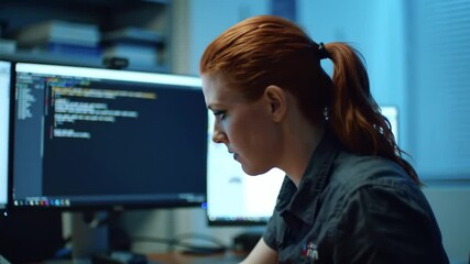 Focused redhead programmer working diligently on code at her workstation