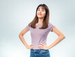 © Daniel - Confident Asian woman standing with hands on hips, smiling with pride and satisfaction, wearing a purple t-shirt and jeans against a clean studio background