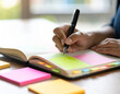 © Bayu - Close-up of a Person Writing in a Notebook with Sticky Notes