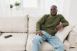 © SHOTPRIME STUDIO - Young African man relaxing on a beige sofa in casual green sweater and blue jeans, looking calm and confident, in a bright modern living room