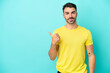 © luismolinero - Young caucasian man isolated on blue background pointing to the side to present a product