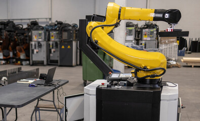 yellow robotic arm lifting object in factory setting with laptop