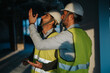 © qunica.com - Two construction supervisors wearing safety vests and helmets inspecting a building site with intent. The scene is lit with natural and indoor lighting, highlighting their professional activity.