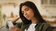 © Yuliia - Boring sad upset frustrated stressed Arabian woman Indian girl female Hispanic lady exhausted sorrowful disappointed holding mobile phone smartphone unwanted pregnancy problem thinking at home couch