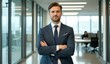 © jiale - Confident businessman in a modern office hallway with arms crossed.
