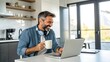 © MdYasin - Smiling Bearded Man Using Laptop in Kitchen Drinking Coffee