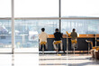 © ilyaska - Travelers working on laptops and waiting for their flights in a bustling airport terminal, surrounded by modern amenities and fellow passengers
