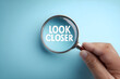 © utaem2022 - Hand holding magnifying glass showing look closer text on blue background