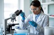 © GraphixStudio - A female scientist uses a pipette to add a sample to a petri dish while using a microscope in a lab