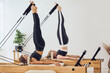 © Sanja - Two young people lying on pilates reformer bed and practicing candle pose at pilates class in bright and airy modern studio.