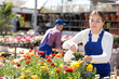 © JackF - Young woman seller in uniform sprays water on flower buds in flower shop